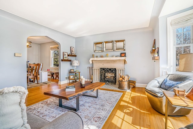 living room with baseboards, arched walkways, wood finished floors, and a fireplace