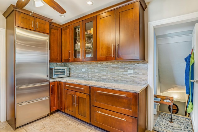 kitchen featuring tasteful backsplash, a toaster, stainless steel built in fridge, and light stone countertops