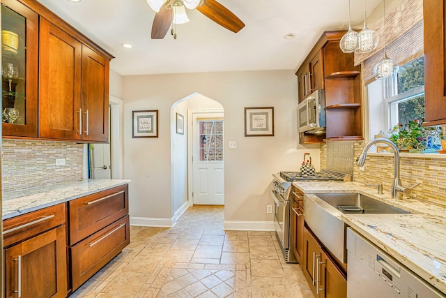 kitchen featuring baseboards, light stone counters, appliances with stainless steel finishes, arched walkways, and a ceiling fan