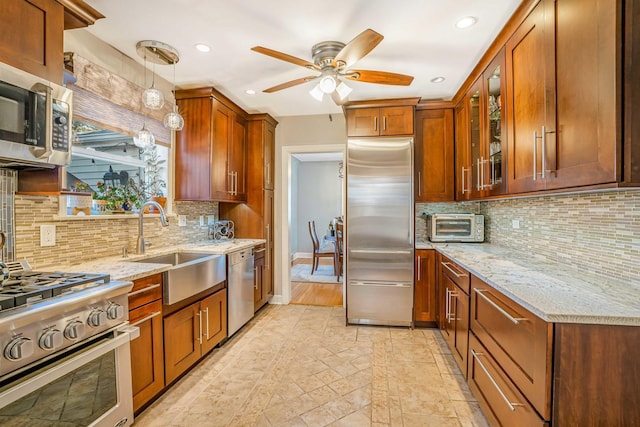 kitchen featuring a ceiling fan, light stone countertops, a sink, glass insert cabinets, and appliances with stainless steel finishes