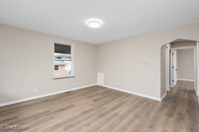 empty room with baseboards, visible vents, arched walkways, and wood finished floors