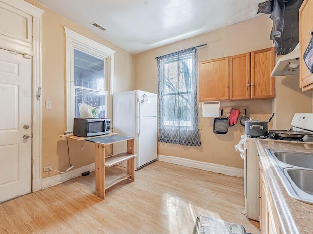 kitchen featuring light countertops, light wood-type flooring, white appliances, under cabinet range hood, and baseboards