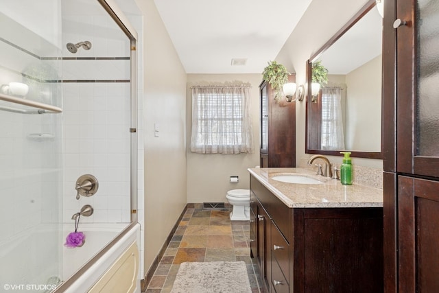 full bath with plenty of natural light, toilet, vanity, and stone tile floors