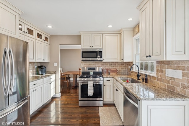 kitchen with tasteful backsplash, appliances with stainless steel finishes, dark wood-type flooring, light stone countertops, and a sink