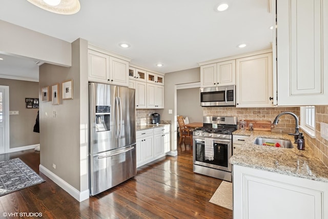 kitchen with light stone counters, dark wood-style floors, stainless steel appliances, a sink, and baseboards