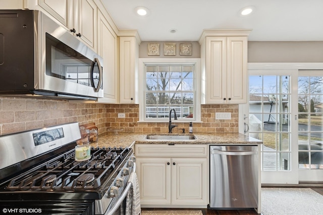 kitchen featuring light stone counters, cream cabinets, appliances with stainless steel finishes, a healthy amount of sunlight, and a sink