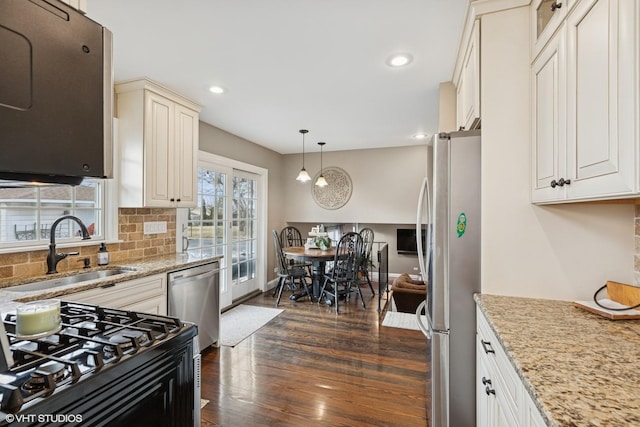 kitchen with dark wood finished floors, stainless steel appliances, backsplash, a sink, and light stone countertops