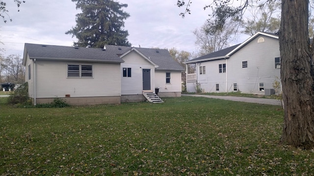 back of house with entry steps, roof with shingles, a lawn, and cooling unit