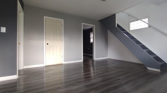 unfurnished living room featuring baseboards, stairway, and wood finished floors