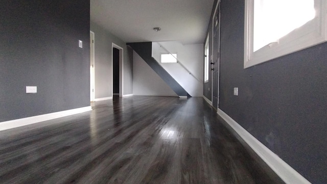 unfurnished living room featuring stairs, dark wood-type flooring, and baseboards