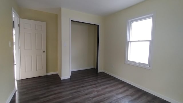 unfurnished bedroom with dark wood-type flooring, a closet, and baseboards