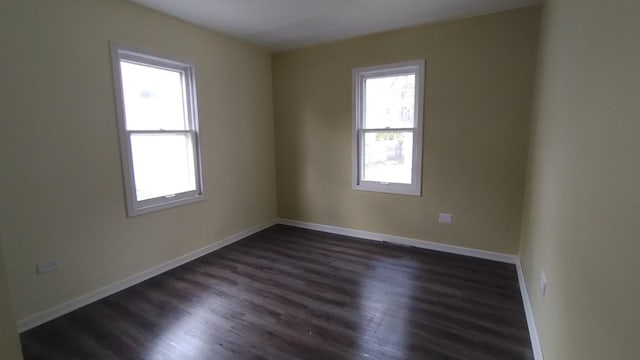 spare room featuring baseboards and dark wood-type flooring