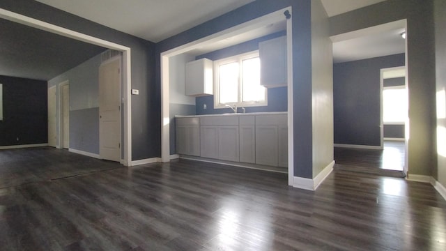 empty room with dark wood-style flooring, a sink, and baseboards