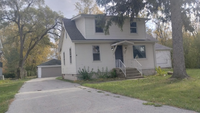 view of front of house with an outbuilding, a front lawn, roof with shingles, and a detached garage