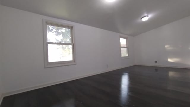 spare room featuring vaulted ceiling, dark wood-style floors, and baseboards