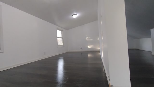 spare room featuring dark wood-type flooring, vaulted ceiling, and baseboards