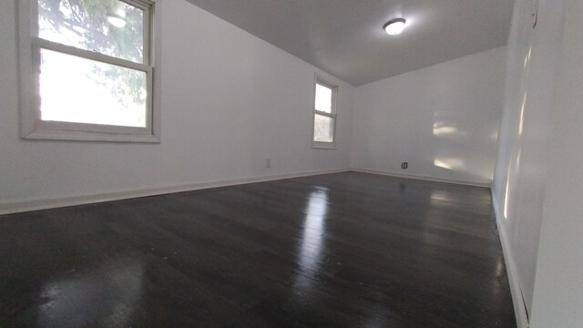 unfurnished room featuring lofted ceiling, baseboards, and wood finished floors