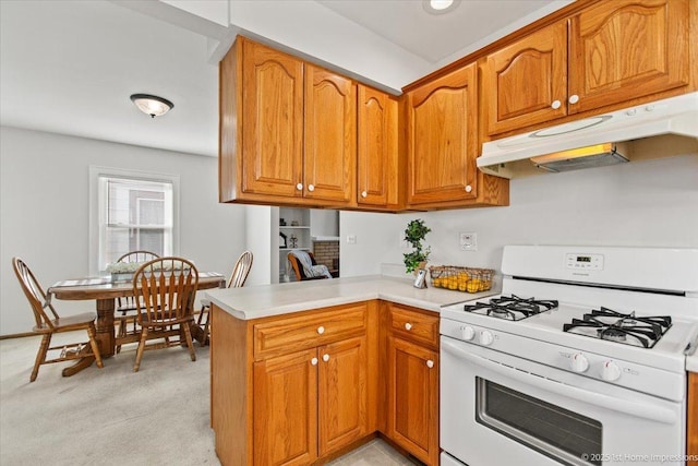 kitchen featuring a peninsula, under cabinet range hood, white range with gas stovetop, and brown cabinetry