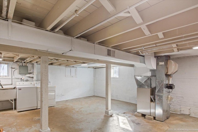 basement with heating unit, washing machine and clothes dryer, visible vents, a sink, and electric panel