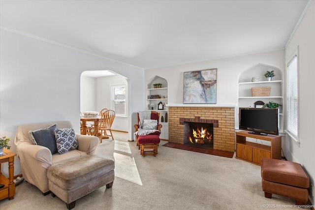 living area featuring arched walkways, carpet floors, built in features, a brick fireplace, and crown molding