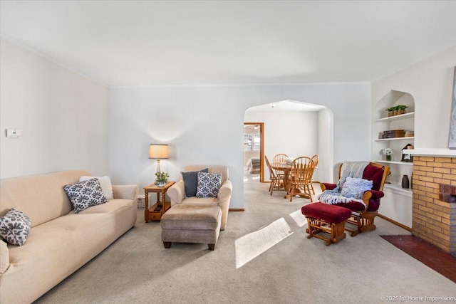 carpeted living area featuring a fireplace, built in features, arched walkways, and crown molding