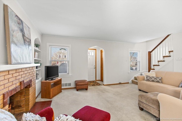 carpeted living area featuring visible vents, arched walkways, baseboards, stairway, and a brick fireplace