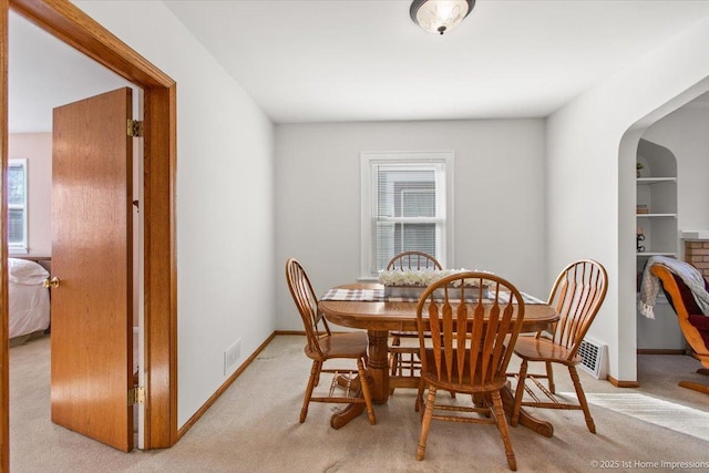 dining room with light colored carpet, arched walkways, visible vents, and baseboards