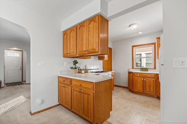 kitchen with light countertops, arched walkways, brown cabinets, and white gas range