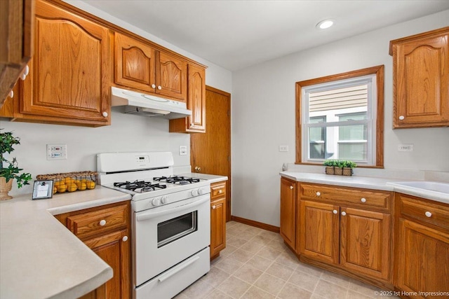 kitchen with under cabinet range hood, white gas range oven, brown cabinets, and light countertops