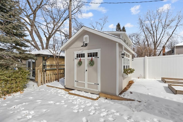 snow covered structure with an outbuilding, a storage shed, and fence