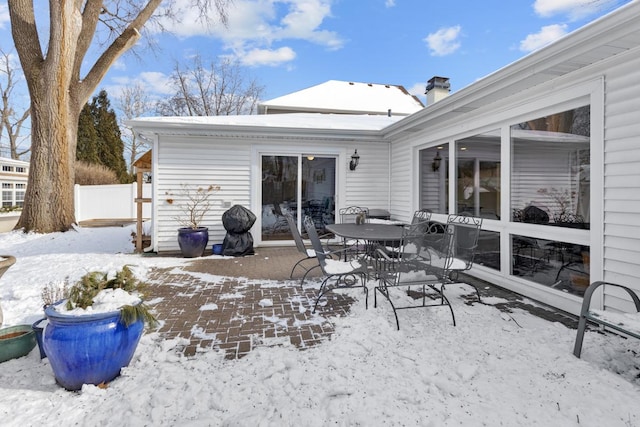 snow covered rear of property with a patio, a chimney, and fence