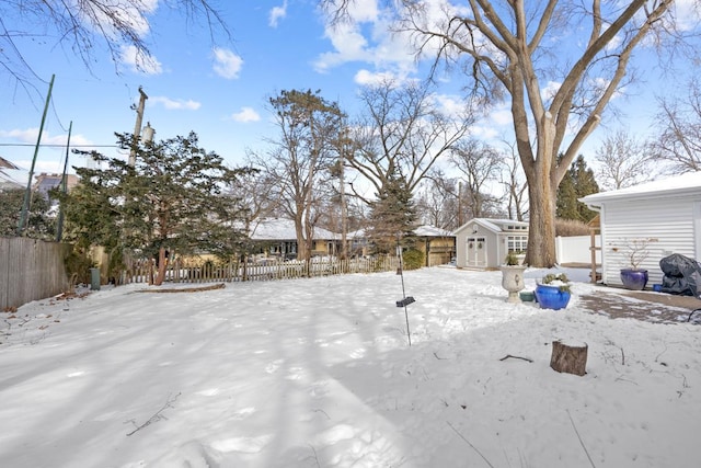 snowy yard with a storage shed, a fenced backyard, and an outbuilding