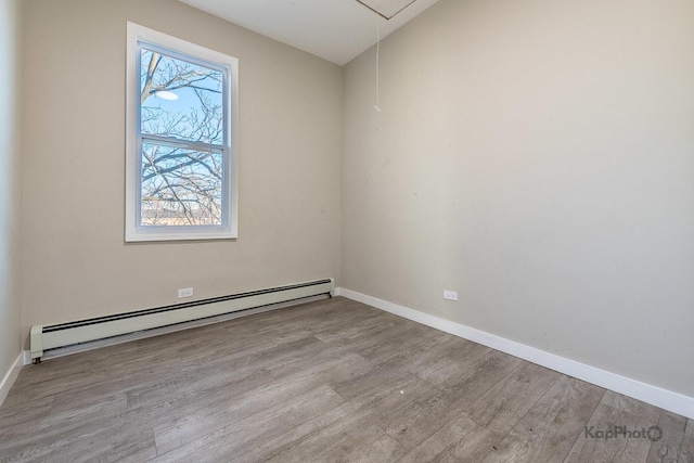 spare room with a baseboard heating unit, attic access, baseboards, and wood finished floors