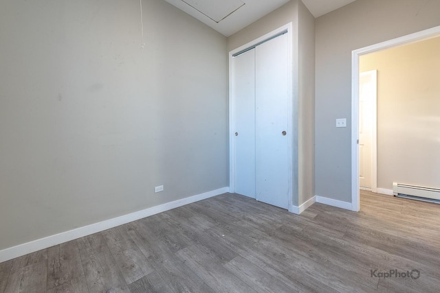 unfurnished bedroom with a closet, baseboards, baseboard heating, and wood finished floors