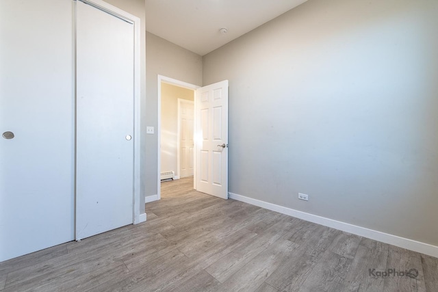 unfurnished bedroom with a closet, baseboards, baseboard heating, and wood finished floors