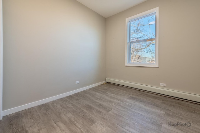 spare room featuring a baseboard radiator, baseboards, and wood finished floors