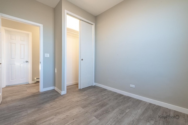 unfurnished bedroom featuring a baseboard heating unit, a closet, wood finished floors, and baseboards