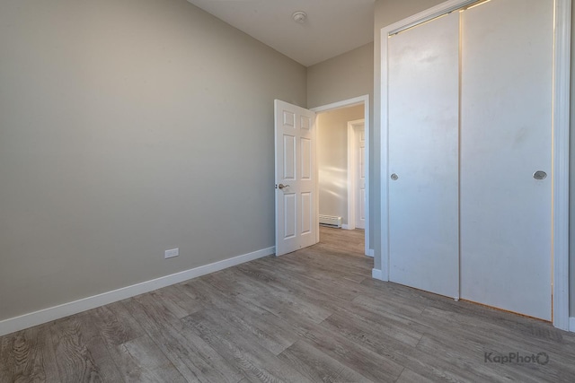 unfurnished bedroom featuring a baseboard heating unit, a closet, baseboards, and wood finished floors