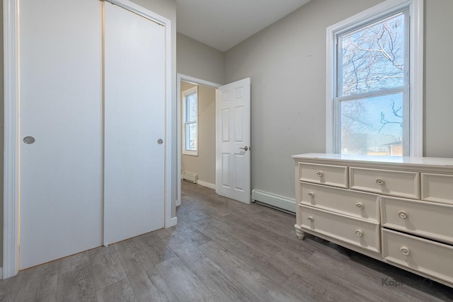 unfurnished bedroom featuring a baseboard radiator, wood finished floors, baseboards, a closet, and baseboard heating