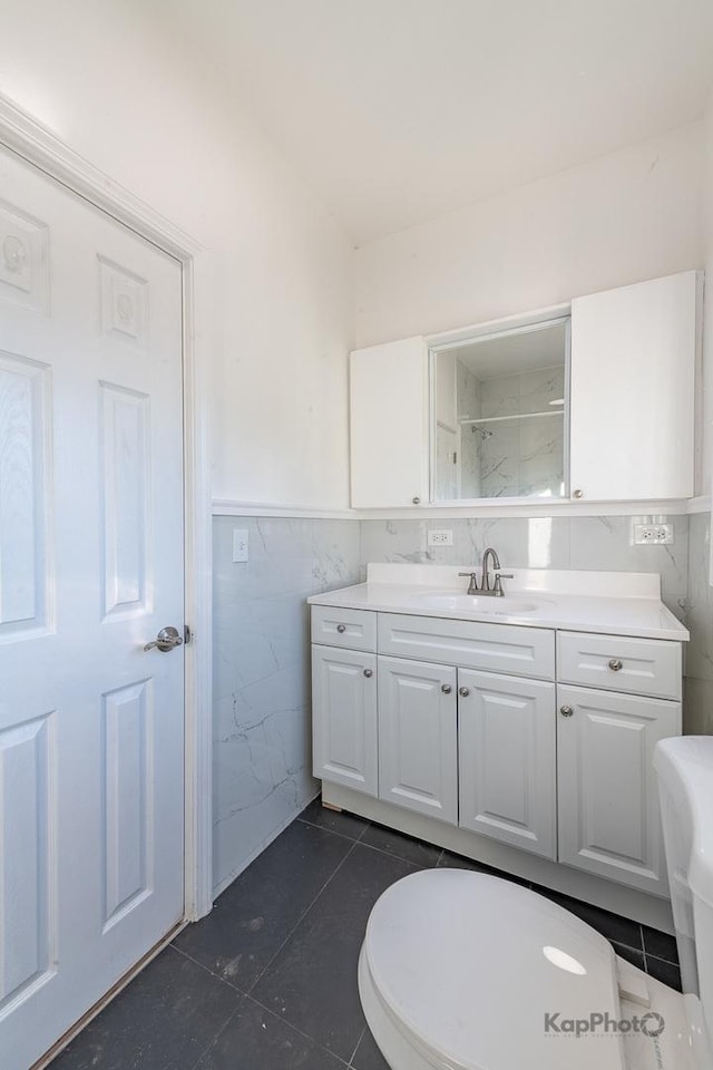 full bath with toilet, a wainscoted wall, tile patterned floors, vanity, and tile walls