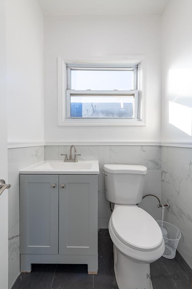 bathroom featuring tile walls, wainscoting, vanity, and toilet