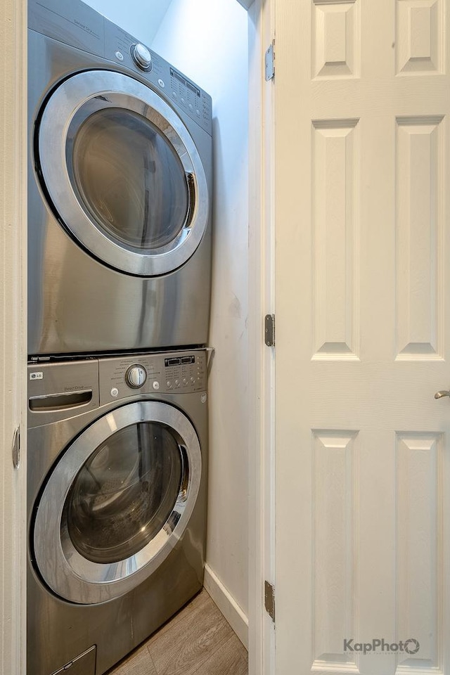 laundry room featuring wood finished floors, stacked washer and clothes dryer, baseboards, and laundry area