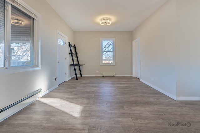 empty room with a baseboard radiator, baseboards, and wood finished floors