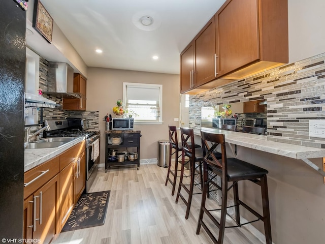 kitchen with stainless steel appliances, brown cabinets, a sink, and wall chimney exhaust hood