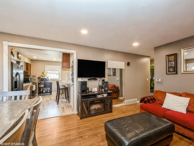 living area featuring baseboards, light wood finished floors, visible vents, and recessed lighting