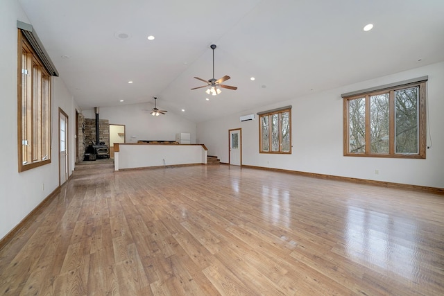 unfurnished living room featuring a wood stove, light wood-type flooring, baseboards, and lofted ceiling