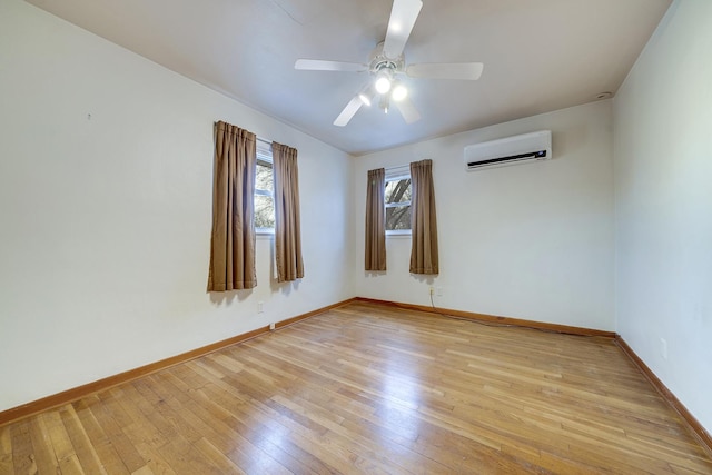 spare room with light wood finished floors, a ceiling fan, baseboards, and an AC wall unit