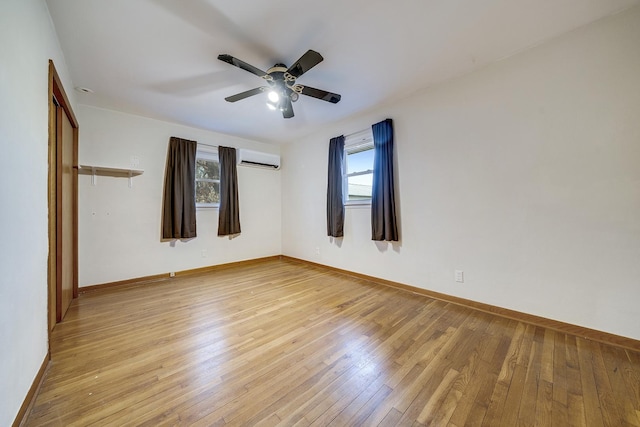 unfurnished bedroom with baseboards, an AC wall unit, a ceiling fan, and light wood-style floors