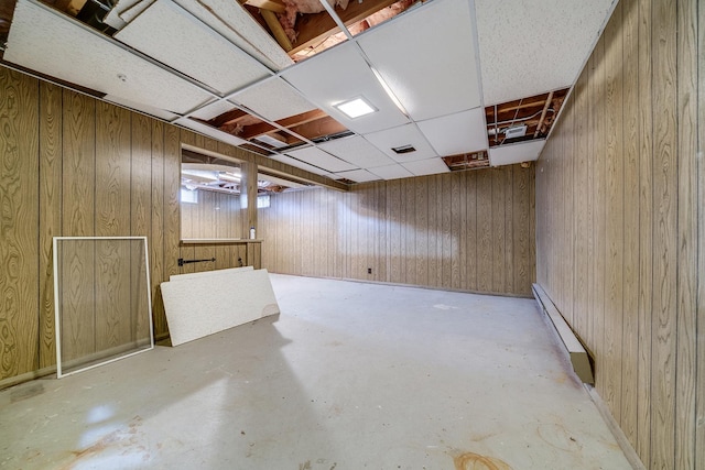 unfinished below grade area featuring a baseboard heating unit, a drop ceiling, and wood walls