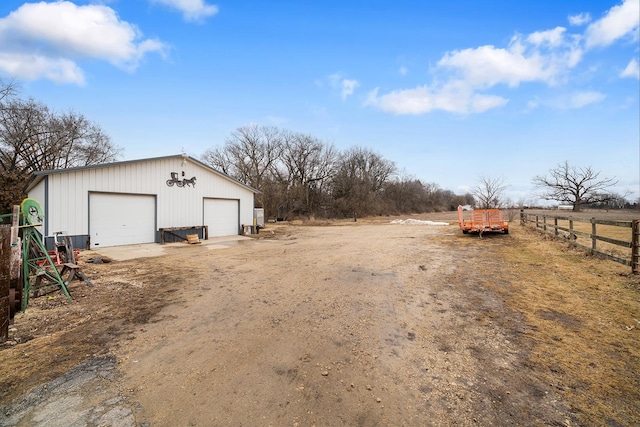 view of yard with a garage, a rural view, fence, and an outbuilding